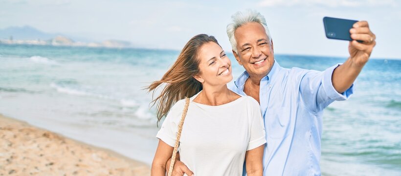 Middle age hispanic couple smiling happy making selfie by the smartphone at the beach.