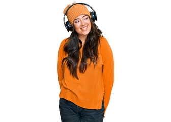 Beautiful brunette young woman listening to music using headphones looking away to side with smile on face, natural expression. laughing confident.