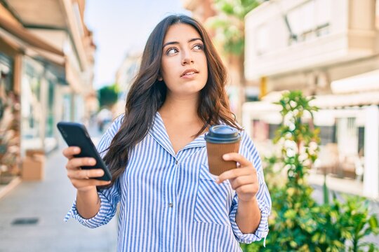 Young hispanic businesswoman using smartphone and drinking take away coffee at the city.
