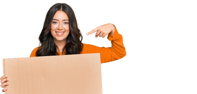 Beautiful brunette young woman holding cardboard blank empty banner pointing finger to one self smiling happy and proud