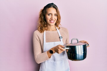 Young caucasian woman wearing apron holding cooking pot smiling with a happy and cool smile on...