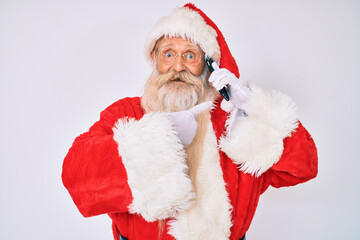 Old senior man wearing santa claus costume speaking on the phone smiling happy pointing with hand and finger