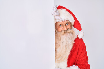 Old senior man with grey hair and long beard wearing santa claus costume holding banner looking positive and happy standing and smiling with a confident smile showing teeth