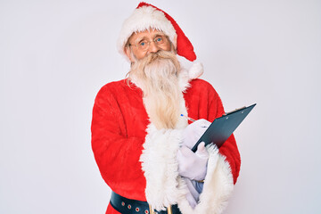 Old senior man with grey hair and long beard wearing santa claus costume writting list smiling with a happy and cool smile on face. showing teeth.