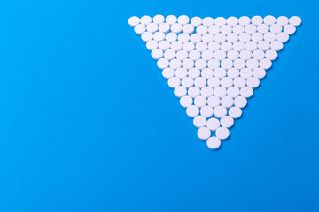 Close up pyramid concept of white pills on blue background with copy space. Focus on foreground, soft bokeh. Pharmacy drugstore concept.