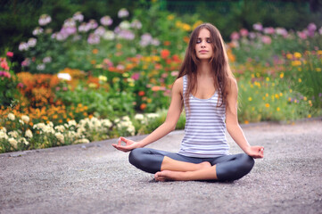 Young caucasian woman practicing yoga on the road in the park at sunset