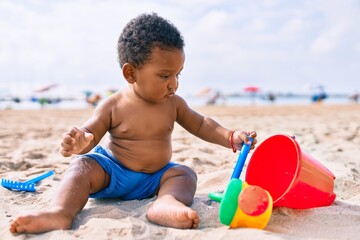 Adorable african american toddler playing with toys sitting on the sand at the beach.