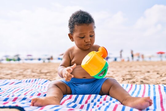 Adorable african american toddler playing with toys sitting on the sand at the beach.