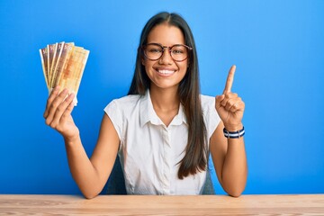 Beautiful hispanic woman holding 500 norwegian krone banknotes smiling with an idea or question...