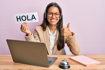 Beautiful hispanic woman wearing operator headset holding hola greenting smiling happy and positive, thumb up doing excellent and approval sign © Krakenimages.com