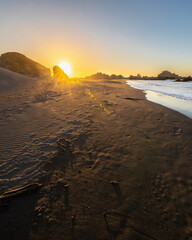 An awe sunset in an idyllic beach landscape with the sunset over the water and the sunlight generating a moody atmosphere. The long shadows of the rocks and the sand generate a texture background