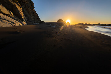 An awe sunset in an idyllic beach landscape with the sunset over the water and the sunlight generating a moody atmosphere. The long shadows of the rocks and the sand generate a texture background