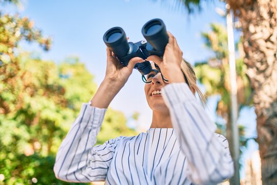 Young blonde businesswoman smiling happy using binoculars at the city.