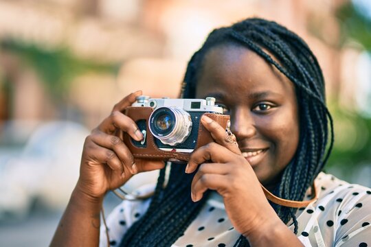 Young african american tourist woman smiling happy using vintage camera at the city.