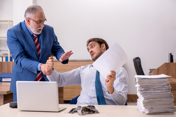 Young male employee and old boss burning papers at workplace