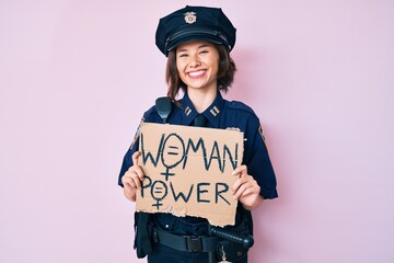 Young beautiful girl wearing police uniform holding woman power banner looking positive and happy...
