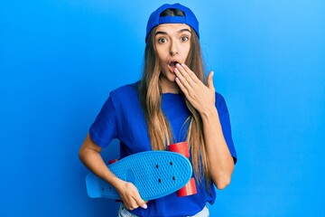 Young hispanic woman holding skate covering mouth with hand, shocked and afraid for mistake....