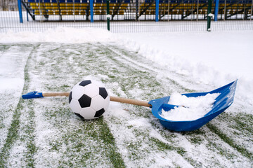 Shovel and classic soccer ball placed on snowy grass of soccer field on winter stadium  © Serhii