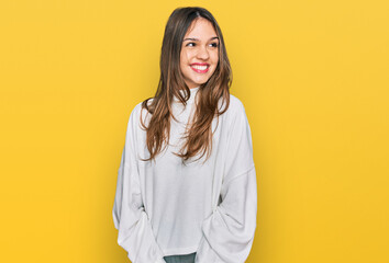 Young brunette woman wearing casual turtleneck sweater looking away to side with smile on face, natural expression. laughing confident.