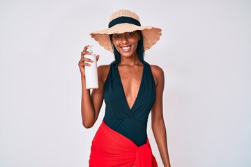 Young african american woman wearing swimsuit and holding sunscreen lotion looking positive and happy standing and smiling with a confident smile showing teeth