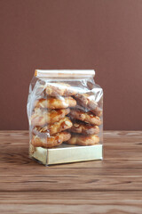 Shortbread cookies with almond flakes in transparent bag on a wooden table against brown wall. Closeup