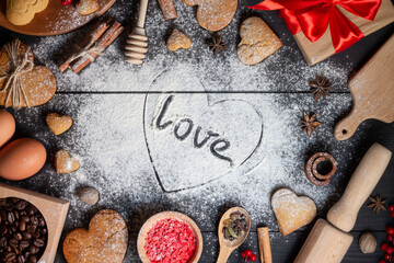 Heart drawn on flour with inscription Love. Gingerbread cookies, spices and baking supplies on black wood background