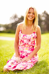 Fototapeta na wymiar Young blond woman in pink dress sitting on the grass in the park