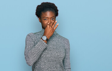 Young african american girl wearing casual clothes smelling something stinky and disgusting,...