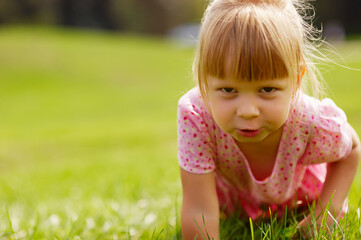 Little blond child girl in a pink dress playing in the grass in the park.