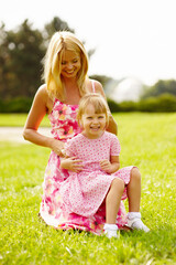 Young blonde mother in dress playing with little kid blonde daughter in the park.