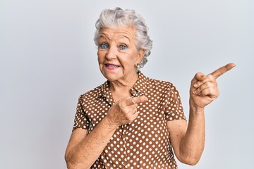 Senior grey-haired woman wearing casual clothes smiling and looking at the camera pointing with two hands and fingers to the side.