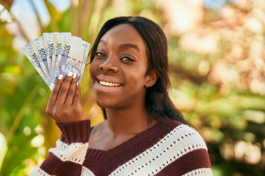 Young african american woman smiling happy holding south africa rands at the park.