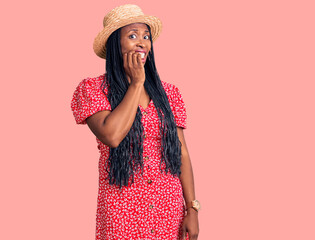 Young african american woman wearing summer hat looking stressed and nervous with hands on mouth biting nails. anxiety problem.