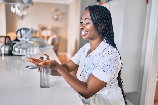Young african american woman smiling happy using sanitizer hand gel at home
