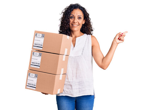 Middle age beautiful woman holding delivery package smiling happy pointing with hand and finger to the side