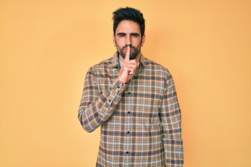Fototapeta premium Handsome hispanic man with beard wearing casual clothes asking to be quiet with finger on lips. silence and secret concept.