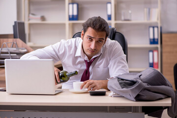 Young male employee drinking alcohol in the office