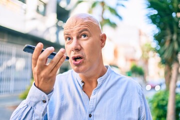 Middle age bald man smiling happy sending audio message using smartphone at the city.