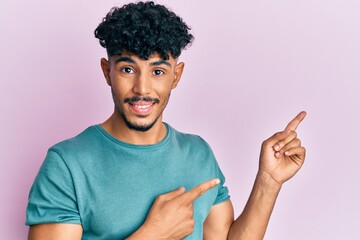 Young arab handsome man wearing casual clothes smiling and looking at the camera pointing with two hands and fingers to the side.