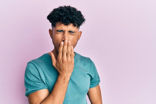 Young arab handsome man wearing casual clothes bored yawning tired covering mouth with hand. restless and sleepiness.