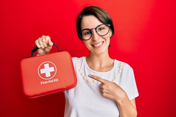 Young brunette woman with short hair holding first aid kit smiling happy pointing with hand and finger