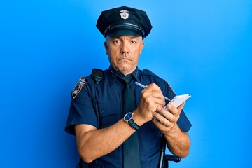 Handsome middle age mature man wearing police uniform writing a ticket relaxed with serious expression on face. simple and natural looking at the camera.