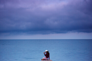 Young caucasian woman in a hat sitting on a pier near the sea.