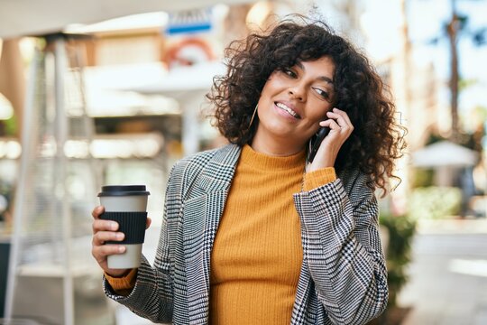 Young hispanic businesswoman talking on the smartphone drinking coffee at the city.