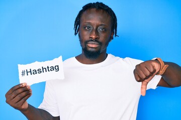 Young african american man with braids holding hashtag paper with angry face, negative sign showing...
