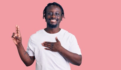 Young african american man with braids wearing casual white tshirt smiling swearing with hand on...
