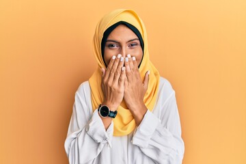 Young brunette arab woman wearing traditional islamic hijab scarf laughing and embarrassed giggle...