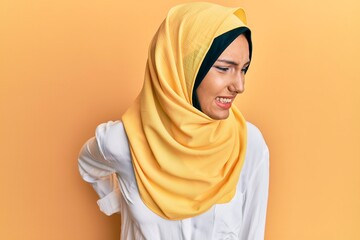 Young brunette arab woman wearing traditional islamic hijab scarf suffering of backache, touching...