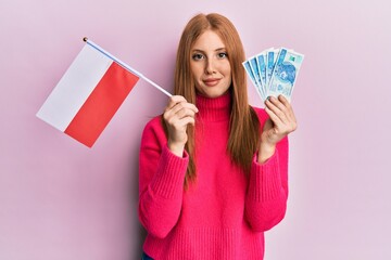 Young irish woman holding poland flag and zloty banknotes relaxed with serious expression on face. simple and natural looking at the camera.