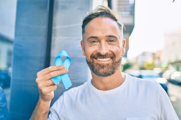 Middle age handsome man smiling happy holding blue prostate cancer ribbon at the city. - obrazy, fototapety, plakaty
